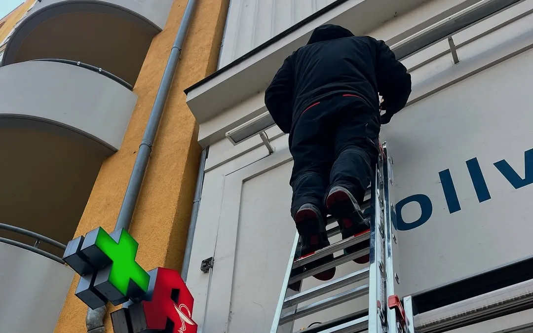 Arbeit an einer Apothekenfassade mit Lichtkreuz und erneuerter Beschriftungsfläche